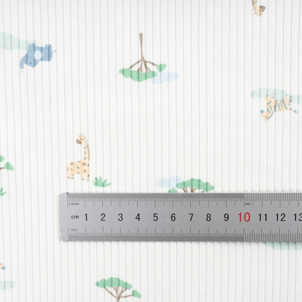 Close-up of a white cloth with fine vertical gray stripes and scattered small animal and tree motifs in muted blue, green, and tan; a ruler lies across the center.