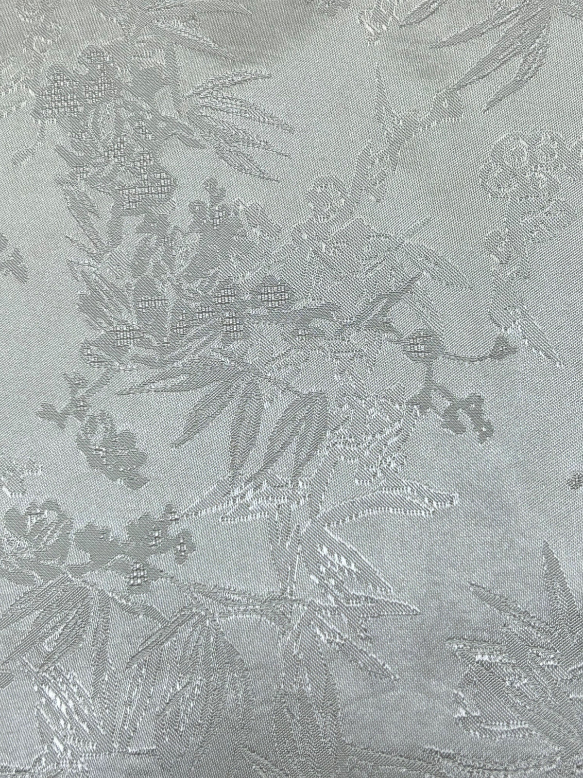 Close-up of pale gray fabric with a subtle woven floral and leafy motif scattered across the surface.
