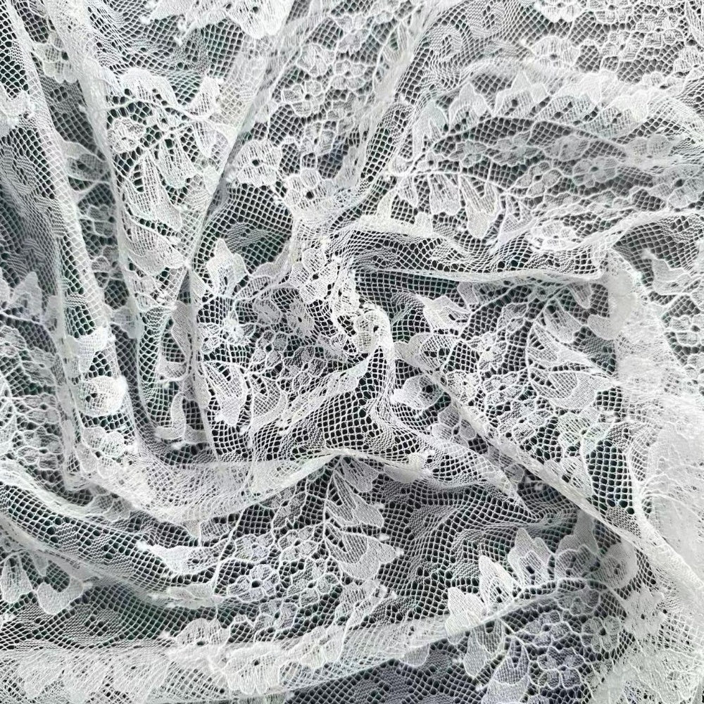 Close-up of white lace with an intricate open mesh and floral motifs, layered in curved drapes.