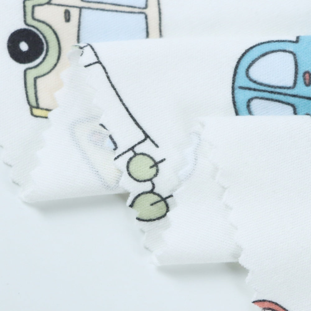 Close-up of white cloth with a black-outlined cartoon vehicle motif in pale green and blue, partly obscured by overlapping draped folds.
