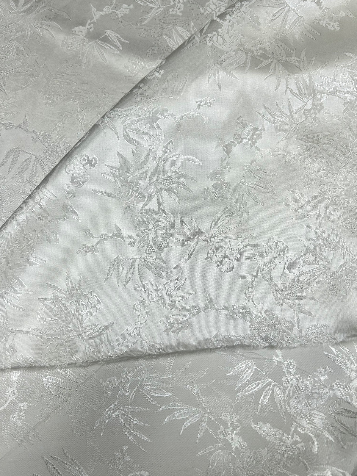 Close-up of folded silvery gray cloth with a subtle tone-on-tone pattern of bamboo leaves, branches, and small blossoms.